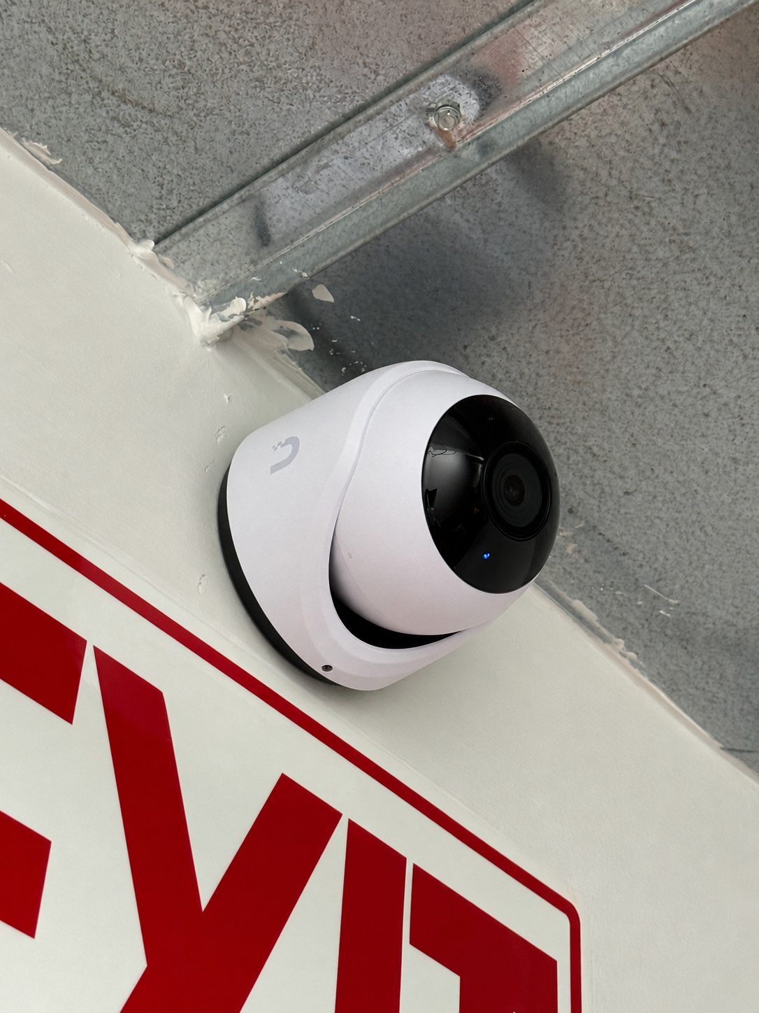 Dome camera covering an exit, mounted to the steel above the sign.